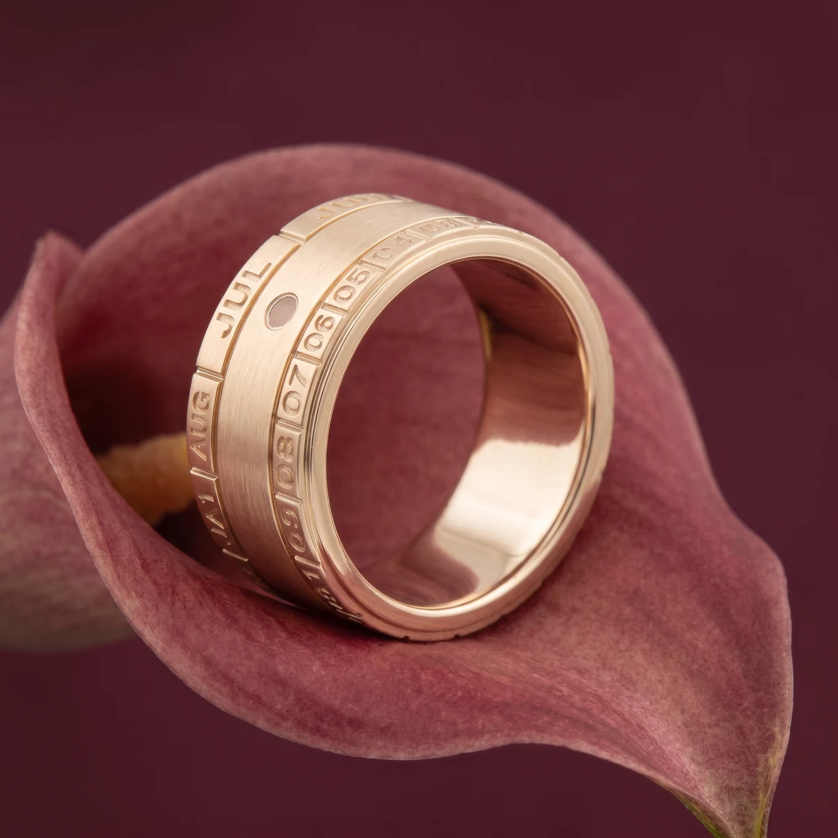 AI design visualization: Calendar Date yellow gold ring resting diagonally on an oxblood calla petal